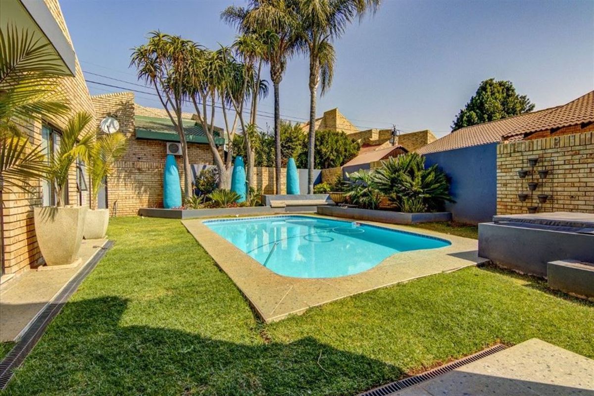 A well-maintained outdoor pool area featuring a clear swimming pool, paved surround, and established garden landscaping within a private brick-walled enclosure.