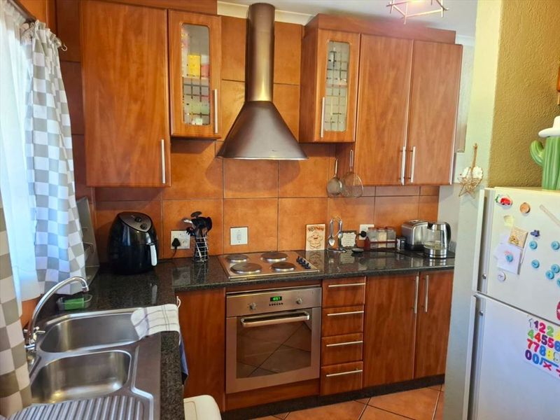 A functional kitchen featuring wooden cabinetry, granite countertops, a built-in oven with electric hob, and a stainless steel extractor fan.