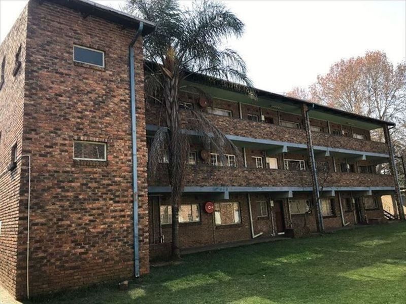 Exterior view of a multi-story apartment building featuring a face brick facade, open balcony walkways, and external stairwell access.