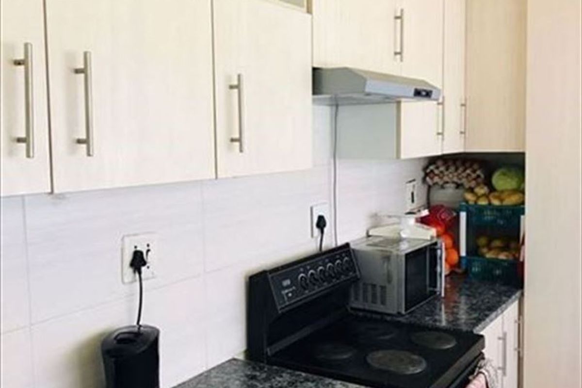 A functional kitchen featuring light-toned cabinetry, dark laminate countertops, a tiled backsplash, and a built-in electric stove with an extractor fan.