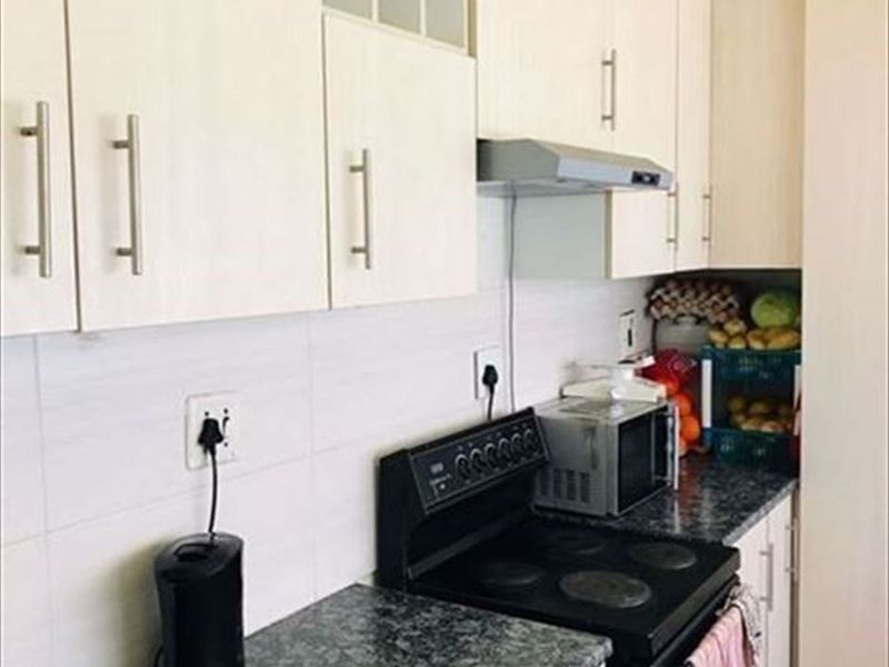 A functional kitchen featuring light-toned cabinetry, dark laminate countertops, a tiled backsplash, and a built-in electric stove with an extractor fan.