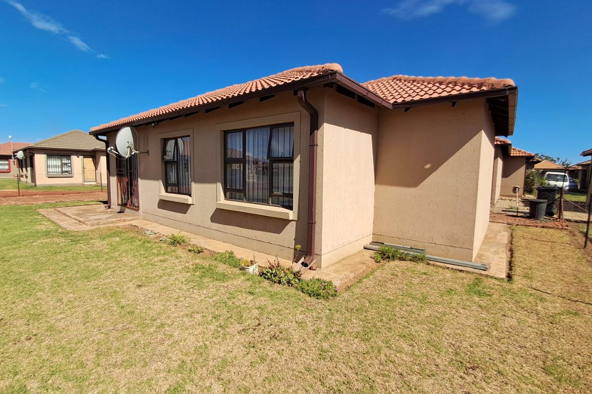 Rear exterior view of a townhouse featuring a tiled roof, security bars on windows, and a surrounding lawn area.