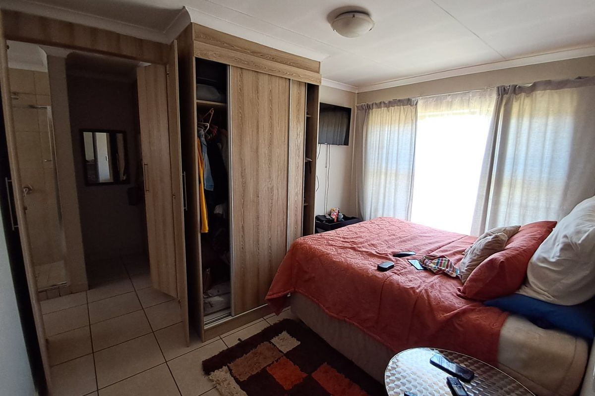 A functional bedroom featuring built-in wooden wardrobes, tiled flooring, and direct access to an en-suite bathroom.