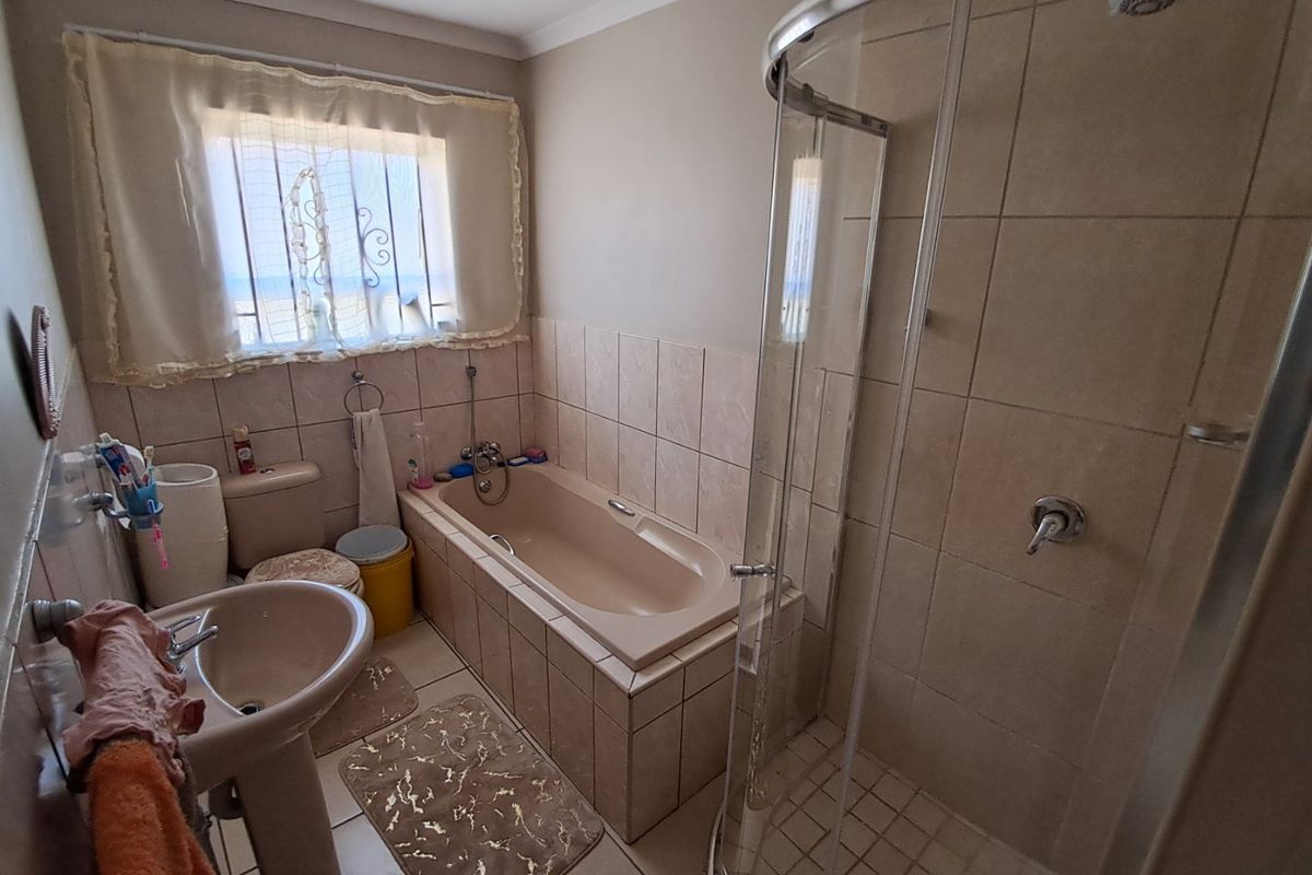 A functional bathroom featuring a pedestal basin, built-in bathtub, and a separate curved glass shower enclosure with neutral wall and floor tiling.