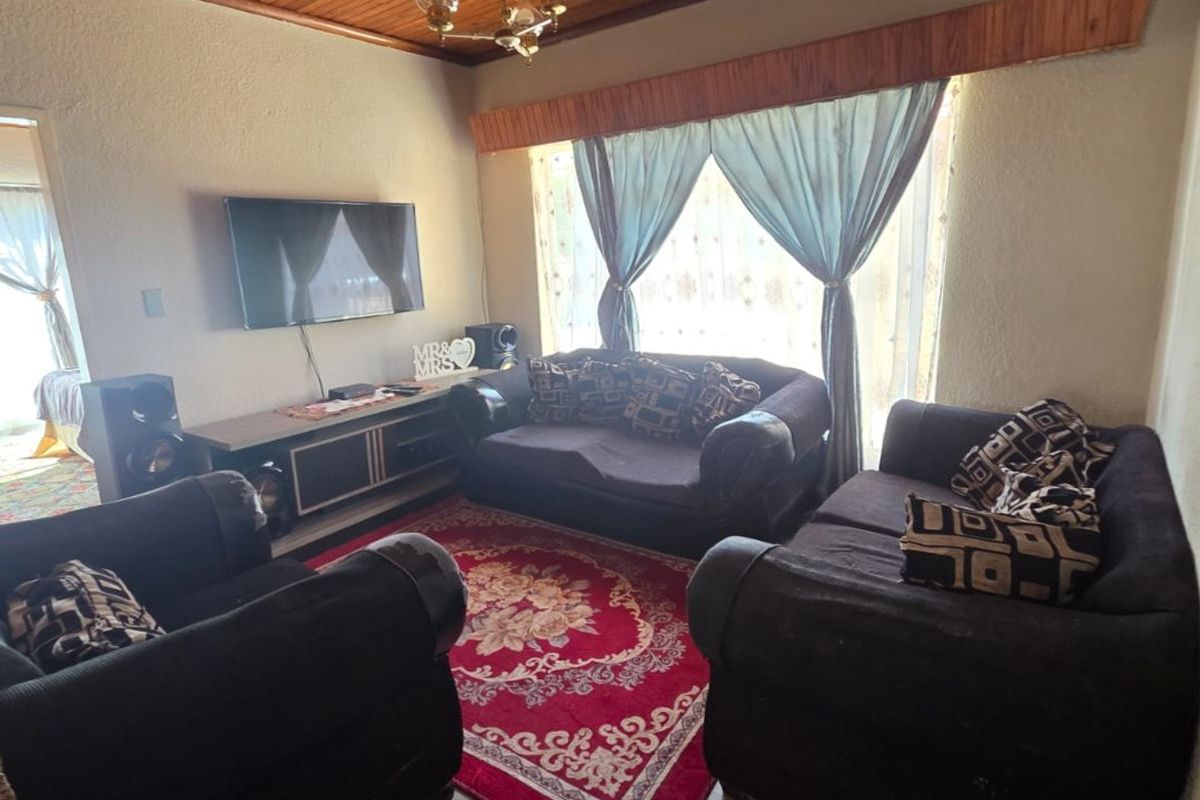 A living room featuring a warm timber tongue and groove ceiling, ceramic floor tiles, and a timber pelmet over the window area.