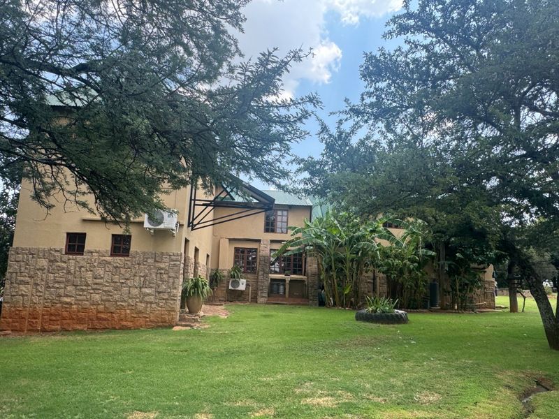 Rear view of a farm-style residence featuring stone cladding, timber window frames, and a well-maintained garden setting with mature trees.
