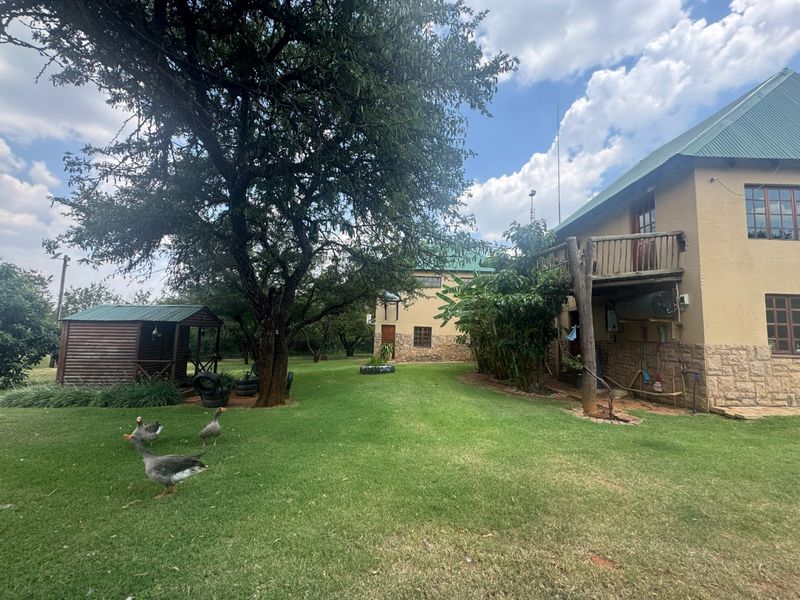 Rear view of the farm property featuring a spacious lawn, mature trees, a timber balcony, and a separate wooden garden shed.