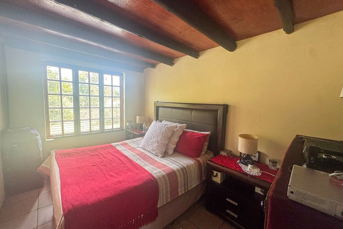 A cozy bedroom featuring exposed timber ceiling beams, tiled flooring, and a multi-pane window providing natural light.