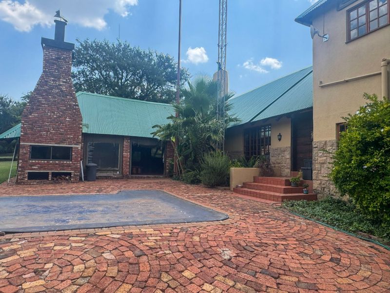 Outdoor entertainment area featuring a brick fireplace, swimming pool with cover, and paved patio space set against the farm house exterior.