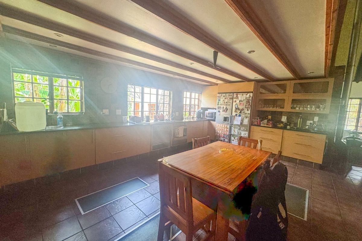 Spacious farmhouse kitchen featuring extensive built-in cabinetry, tiled flooring, and exposed timber ceiling beams, offering a functional layout with ample storage and workspace.