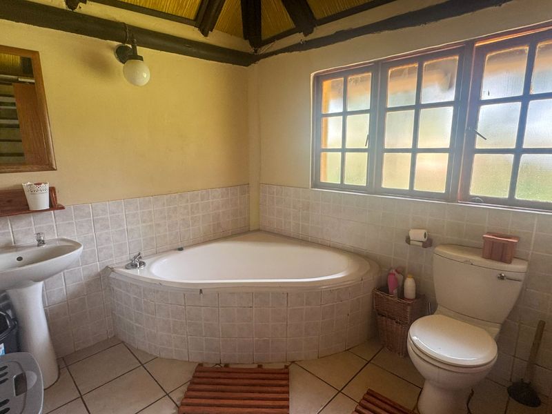 A functional bathroom featuring a corner bathtub, pedestal sink, toilet, and exposed timber ceiling beams, offering a rustic aesthetic with potential for modernization.