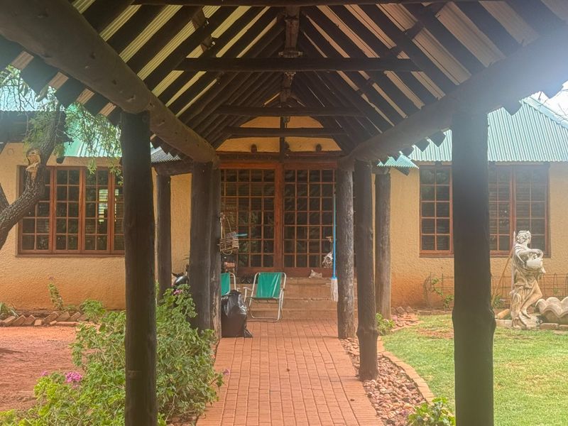A covered outdoor walkway featuring a rustic timber post structure and brick paving, leading to the main entrance of the farm-style dwelling.