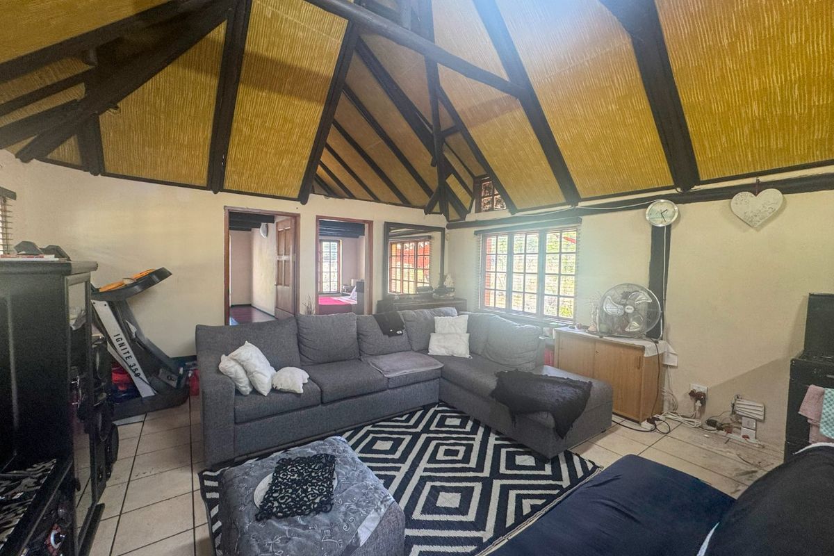 Spacious living room featuring a high vaulted ceiling with exposed timber trusses, thatched roof finish, and tiled flooring.