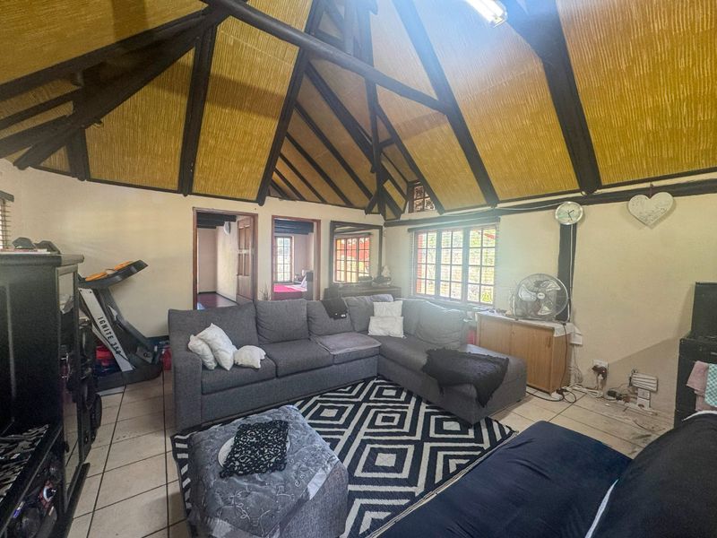 Spacious living room featuring a high vaulted ceiling with exposed timber trusses, thatched roof finish, and tiled flooring.