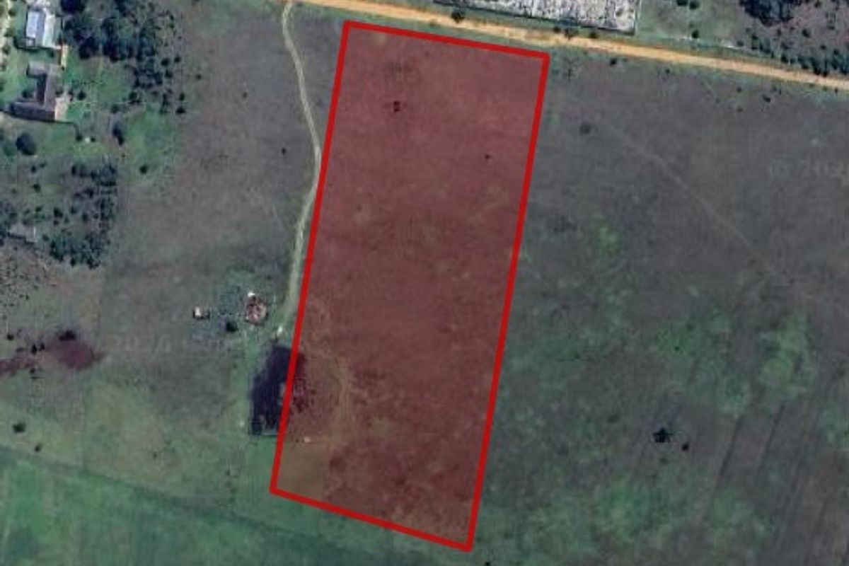 An aerial view of a vacant residential plot of land, highlighted in red, showing the surrounding landscape and access road.