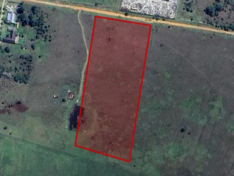 An aerial view of a vacant residential plot of land, highlighted in red, showing the surrounding landscape and access road.