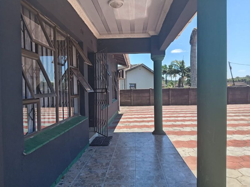 A covered patio area featuring tiled flooring, structural columns, and decorative ceiling detailing, overlooking a paved rear courtyard.