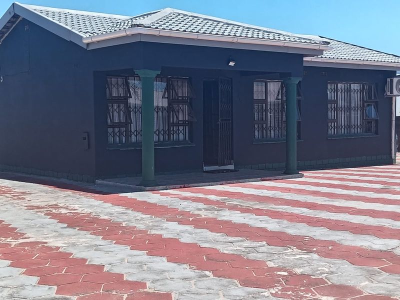 Front elevation of a residential house featuring a covered porch, security bars on windows, and a paved driveway.