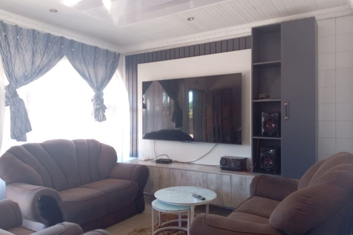 A comfortable living room featuring a built-in media wall unit, recessed ceiling lighting, and tiled flooring.