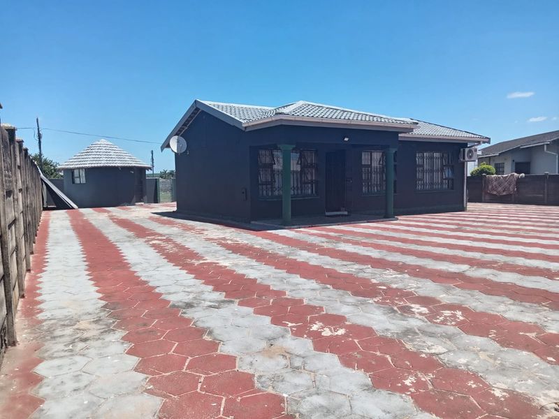 Front view of a detached house featuring a large paved driveway, security gates on windows, and a secondary outbuilding structure.