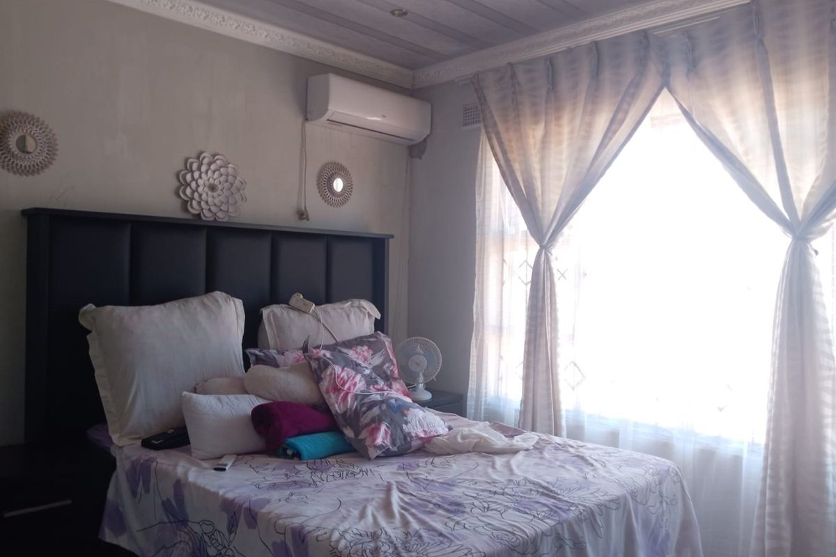 A bedroom featuring a timber panelled ceiling, decorative cornice, and a wall-mounted air conditioning unit with security burglar bars on the window.