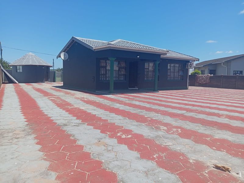 Front view of a detached house featuring a large paved driveway, tiled roof, and a separate outbuilding structure.
