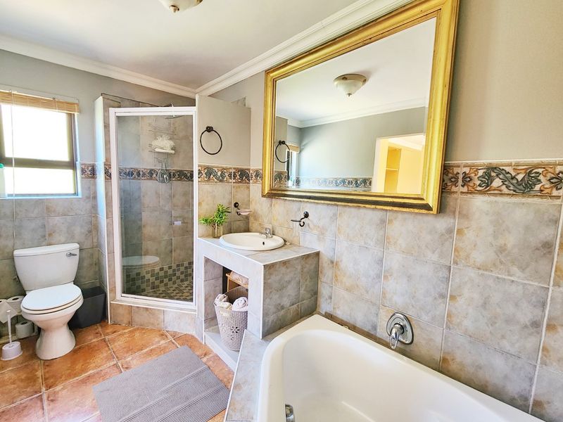 A functional bathroom featuring a tiled shower enclosure, built-in vanity with basin, bathtub, and classic wall tiling throughout.
