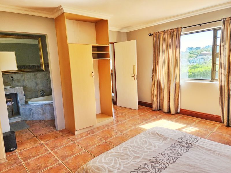 Spacious bedroom featuring tiled flooring, built-in wardrobe, and an open-plan en-suite bathroom with a bathtub, offering natural light and exterior views.
