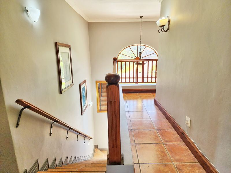 A bright upper-level hallway featuring tiled flooring, a wooden staircase with a matching balustrade, and a distinctive arched window.