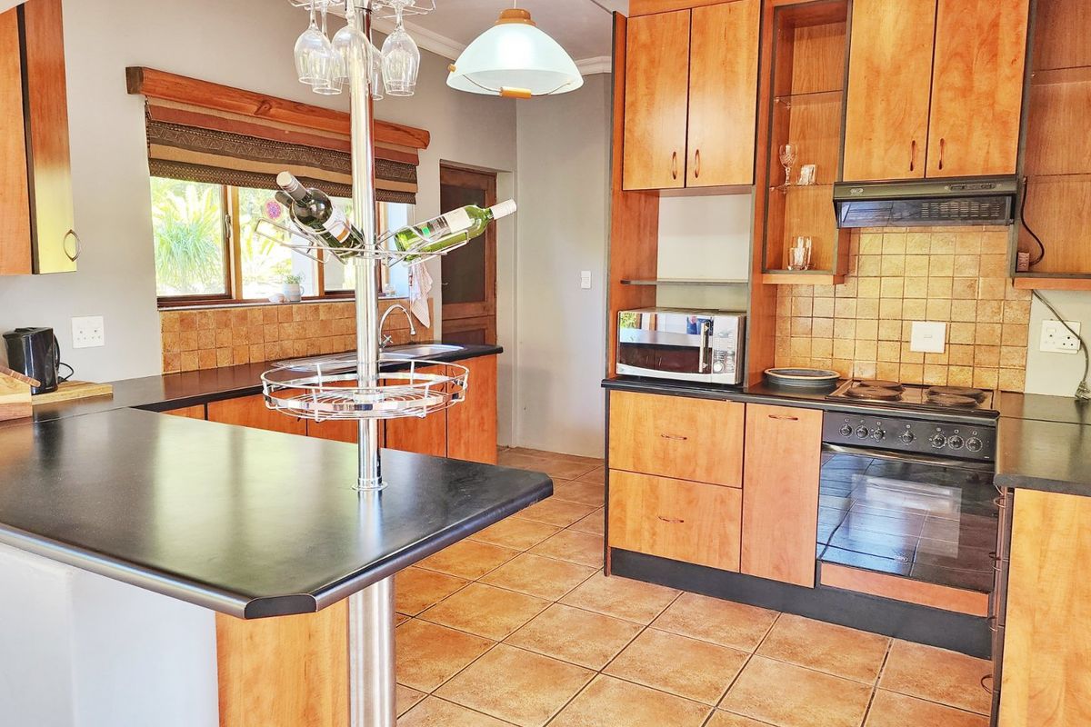 A functional kitchen featuring wooden cabinetry, tiled backsplash, integrated oven and hob, and a breakfast bar counter with tiled flooring.