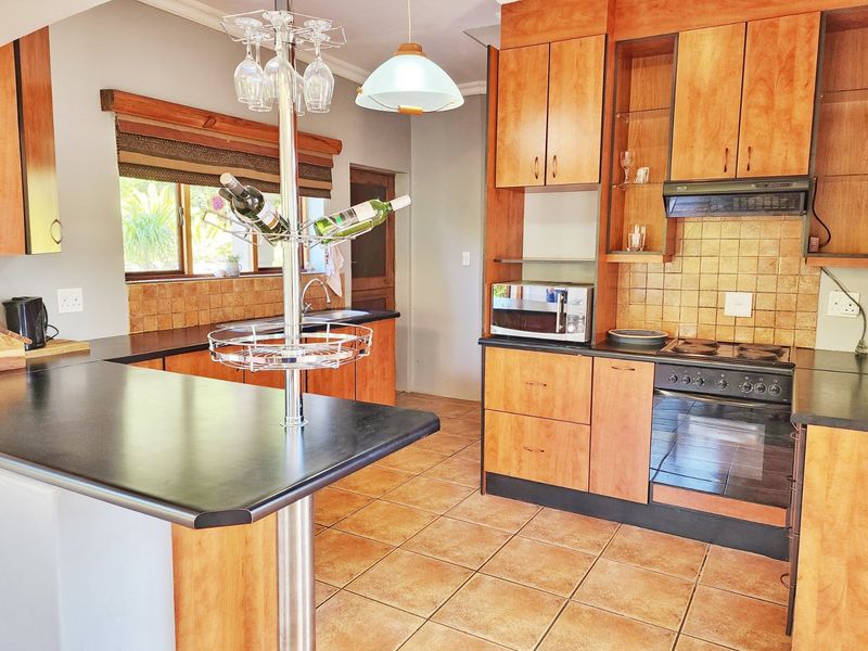 A functional kitchen featuring wooden cabinetry, tiled backsplash, integrated oven and hob, and a breakfast bar counter with tiled flooring.