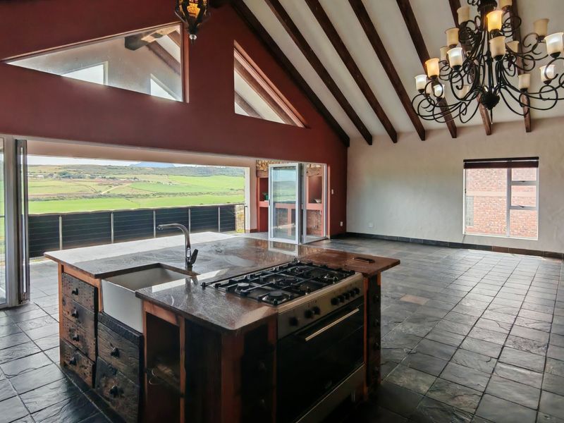 Spacious open-plan living and kitchen area featuring vaulted ceilings with exposed beams, slate flooring, and bi-fold doors opening to scenic countryside views.