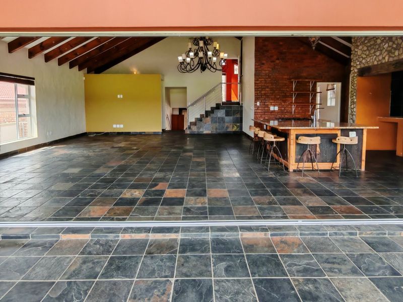 Spacious open-plan living area featuring exposed timber beams, slate flooring, a brick feature wall, and a large kitchen island with built-in cabinetry.