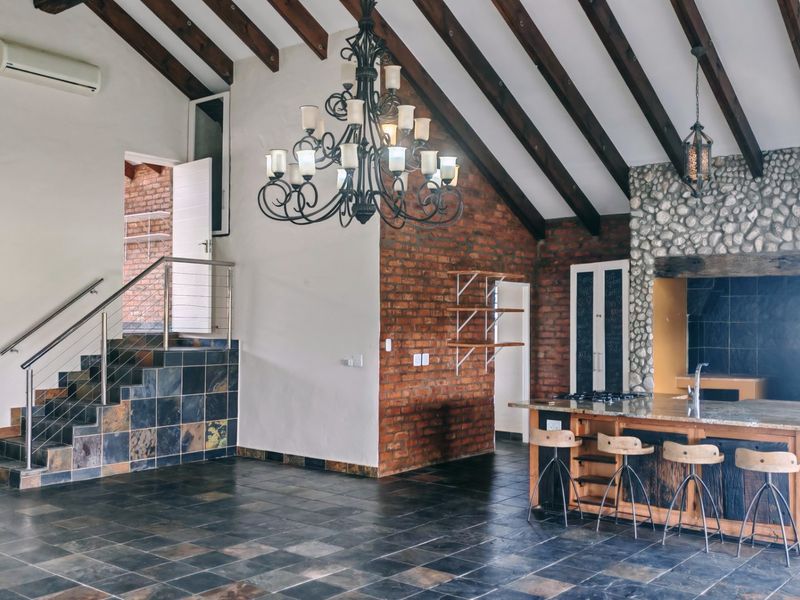 Spacious open-plan living area featuring exposed timber beams, a striking stone fireplace, exposed brickwork, and a large kitchen island with granite countertops.
