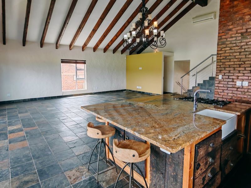 Spacious open-plan living and kitchen area featuring exposed timber beams, a large granite island, and a striking exposed brick wall.