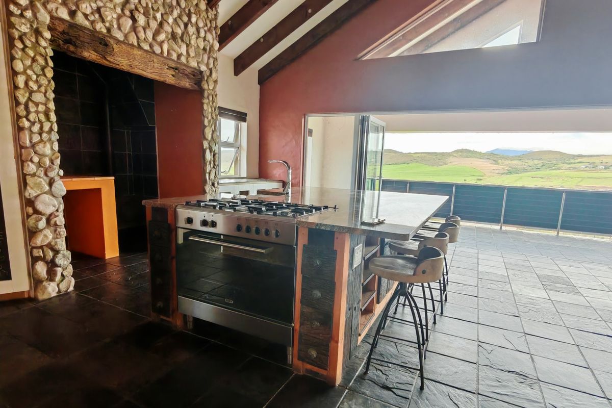 Spacious kitchen featuring a stone-clad fireplace, exposed timber beams, and a central island with a gas stove, opening onto a scenic outdoor patio.
