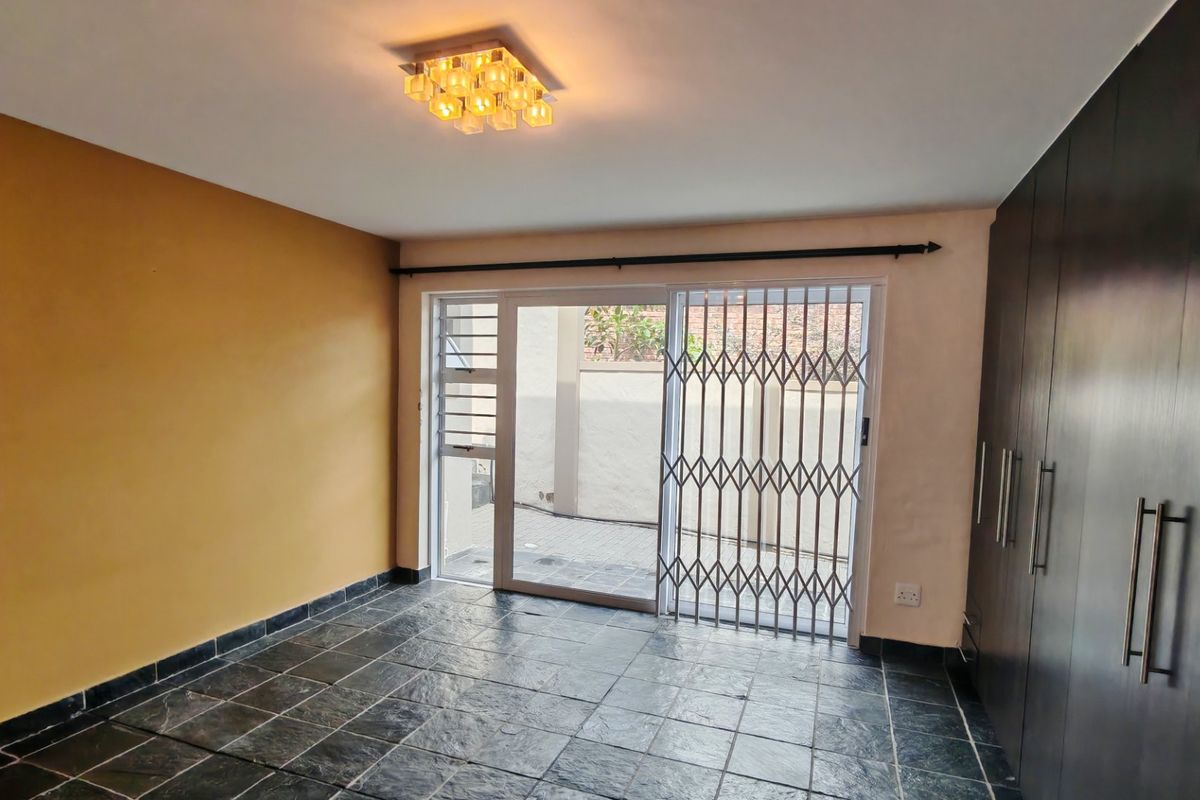 A spacious bedroom featuring dark tiled flooring, built-in cupboards, and a sliding glass door with a security gate leading to the exterior.