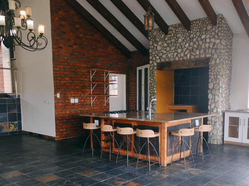 Spacious open-plan living area featuring exposed brick walls, timber beams, a stone fireplace, and a central kitchen island with granite countertops.