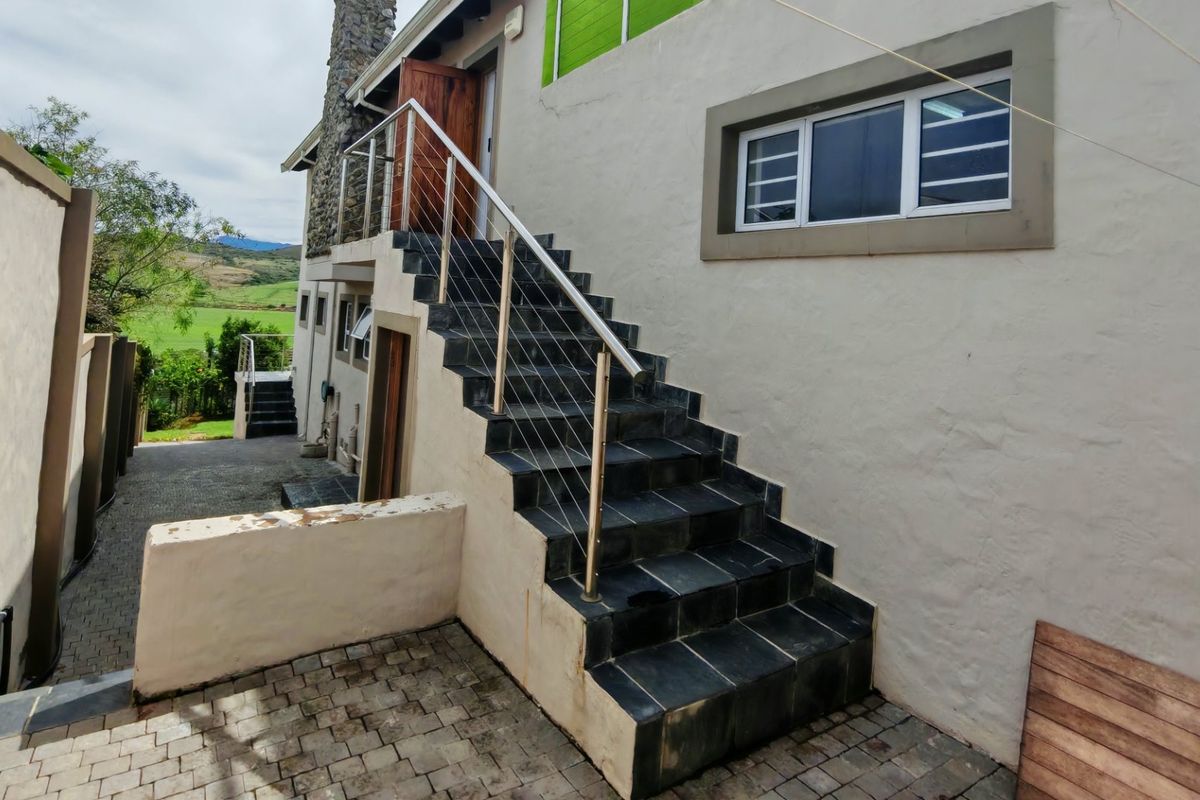 Exterior rear view featuring a stone chimney, tiled staircase with stainless steel balustrade, and paved courtyard area.