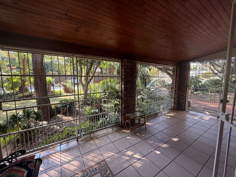 A covered patio area featuring tiled flooring, a timber-clad ceiling, and brick structural pillars, enclosed by security gates overlooking the garden.