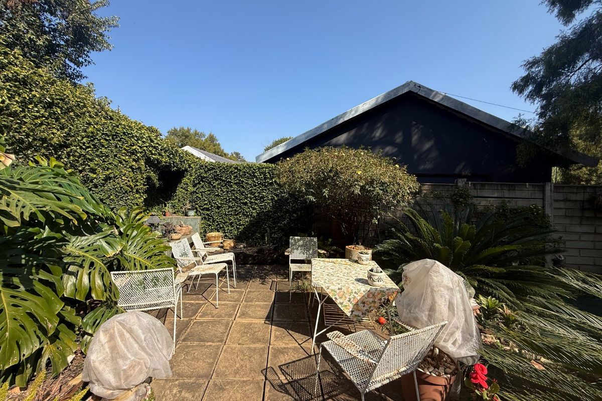 A private rear garden featuring a paved patio area surrounded by established hedging and boundary walls, offering a quiet outdoor space.