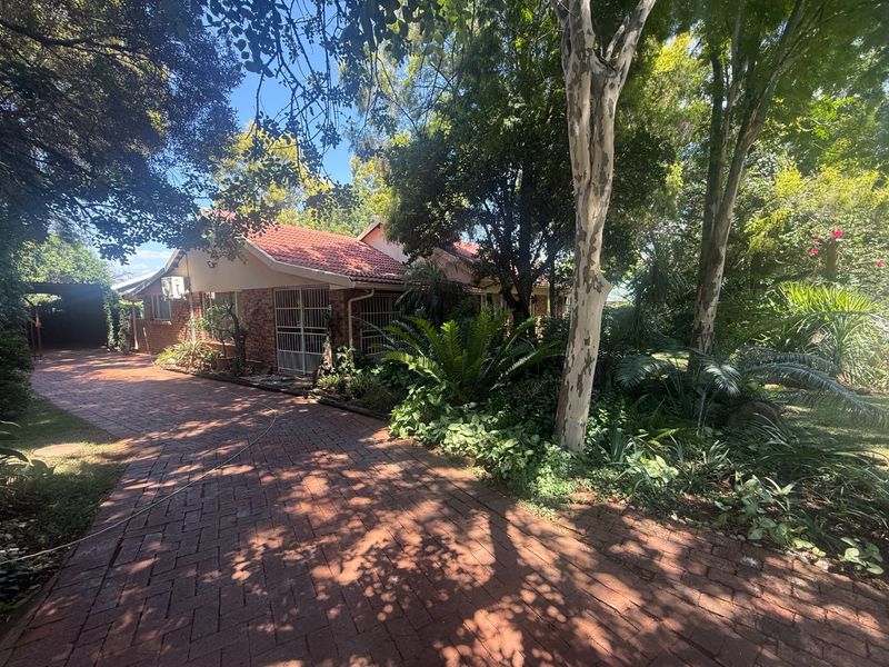 Front view of a brick house featuring a paved driveway, mature garden landscaping, and a tiled roof.
