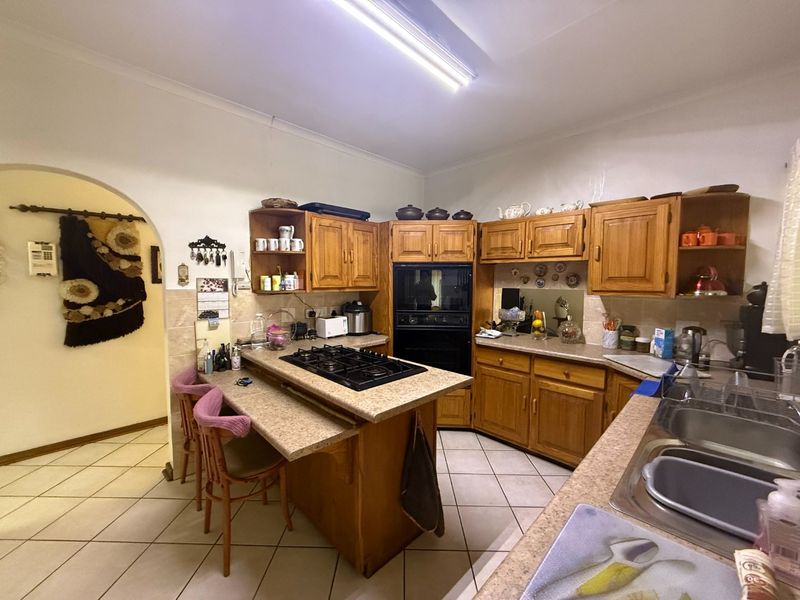 A functional kitchen featuring traditional wooden cabinetry, a built-in oven, gas hob, and laminate countertops with tiled flooring.