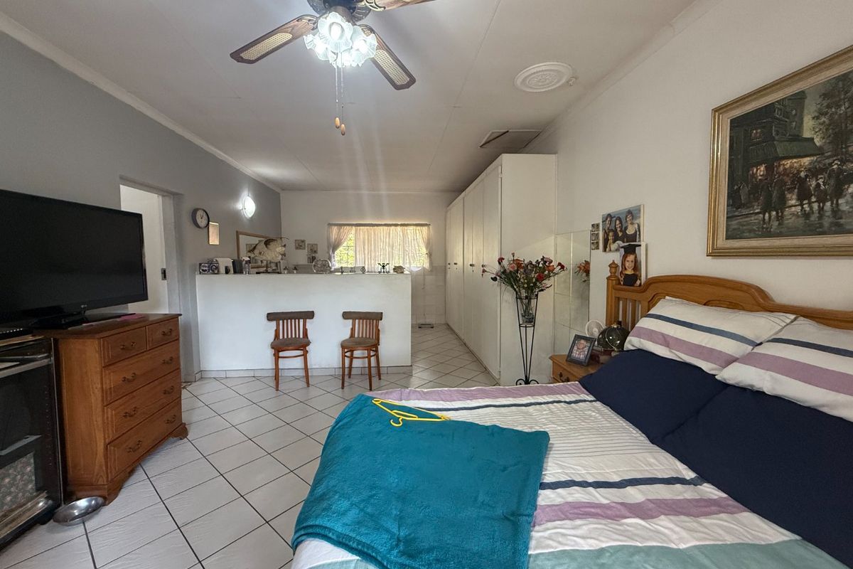 Spacious bedroom featuring tiled flooring, built-in cupboards, and a ceiling fan, with an open-plan layout connecting to a secondary living or utility area.