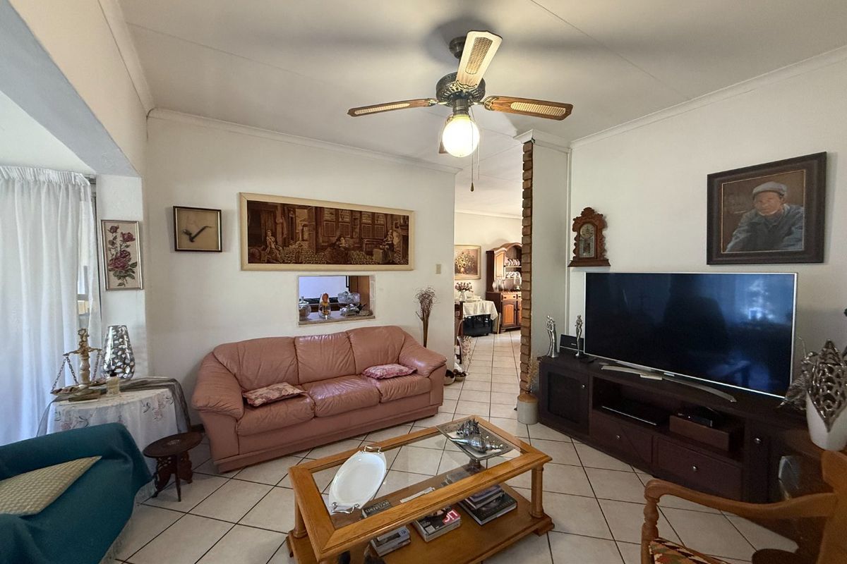 A comfortable living room featuring ceramic floor tiles, a ceiling fan, and a brick feature pillar, with a convenient serving hatch to the kitchen area.