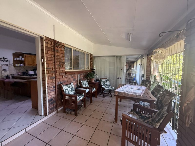A covered patio area featuring tiled flooring, exposed brick walls, and sliding glass doors providing access to the interior living spaces.