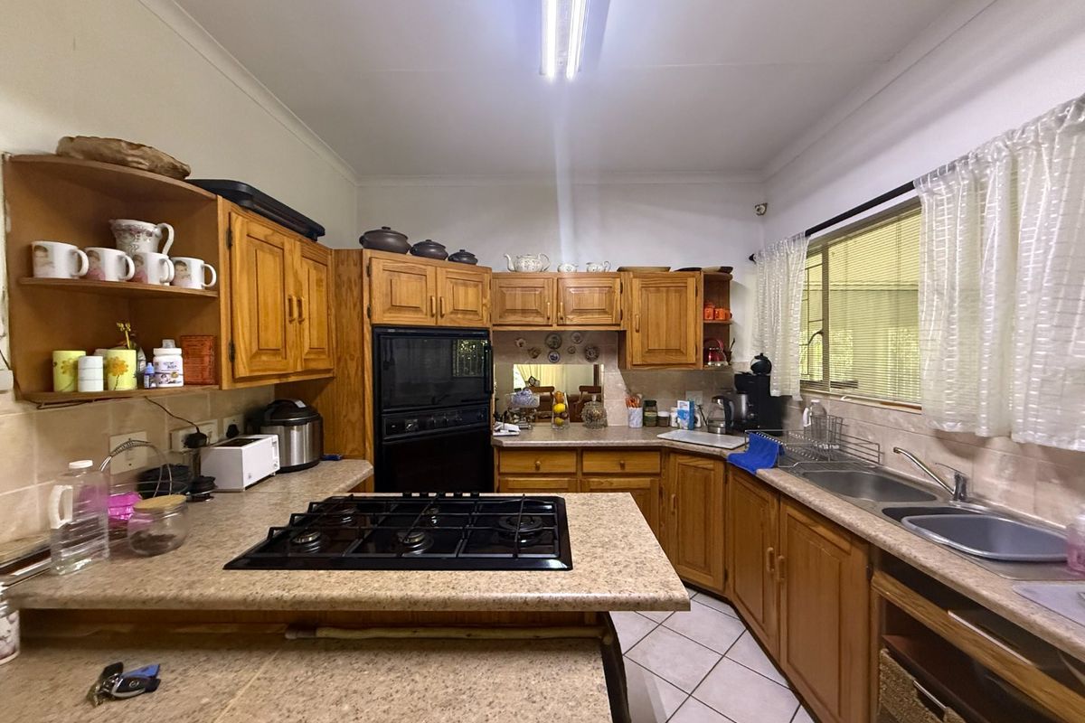 A functional kitchen featuring timber cabinetry, laminate countertops, a gas cooktop, built-in oven, and double bowl sink with tiled flooring.