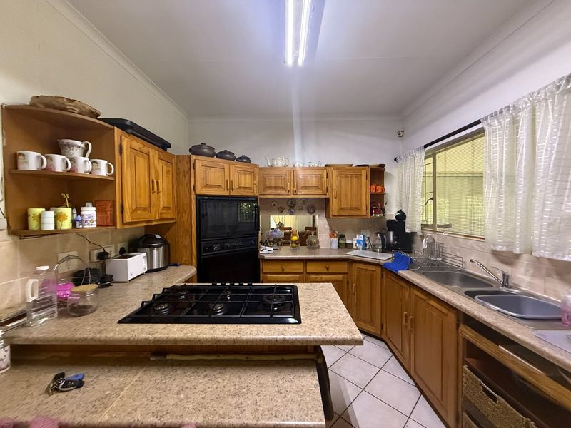 A functional kitchen featuring timber cabinetry, laminate countertops, a gas cooktop, built-in oven, and double bowl sink with tiled flooring.