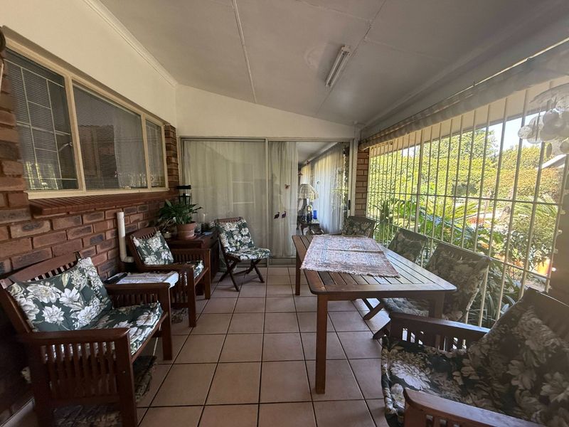 A covered patio area featuring tiled flooring, exposed brick walls, and sliding glass doors leading into the home, secured with metal bars.