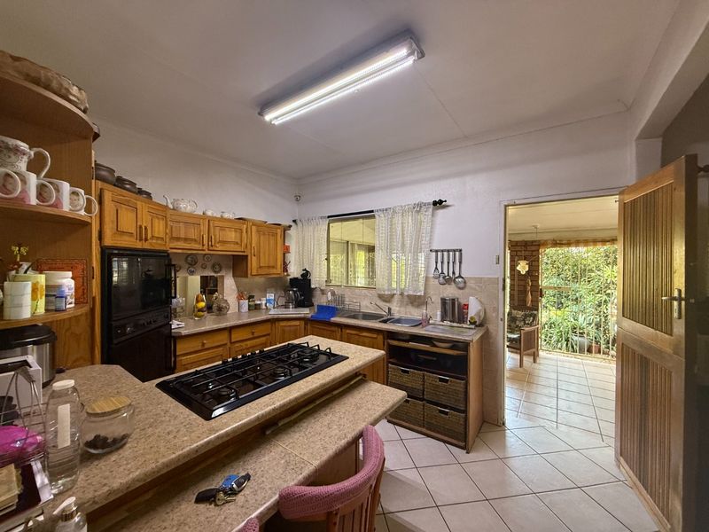 A functional kitchen featuring wooden cabinetry, a built-in gas hob, and tiled flooring, with direct access to an outdoor patio area.